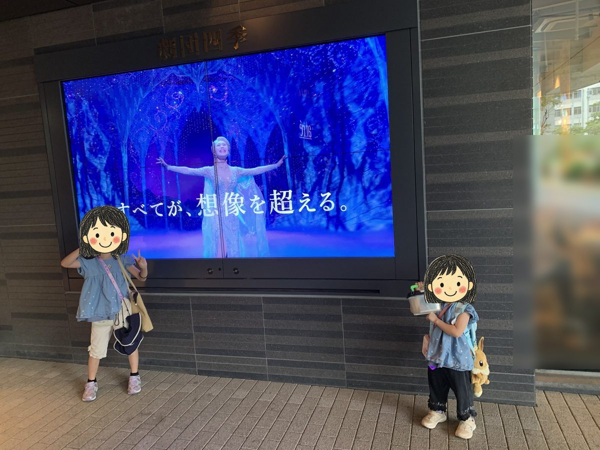 劇場前の大型ディスプレイ「すべてが、想像を超える。」の前に立つ姉妹