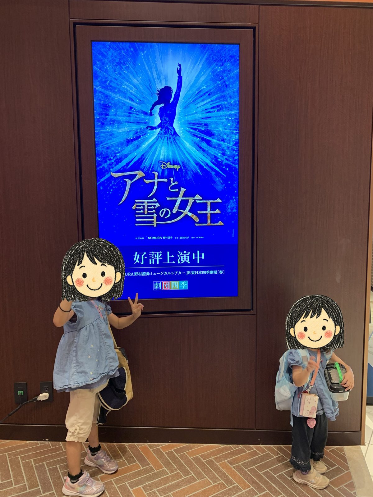 劇場内のデジタルサイネージ「アナと雪の女王 好評上演中」の前に立つ姉妹