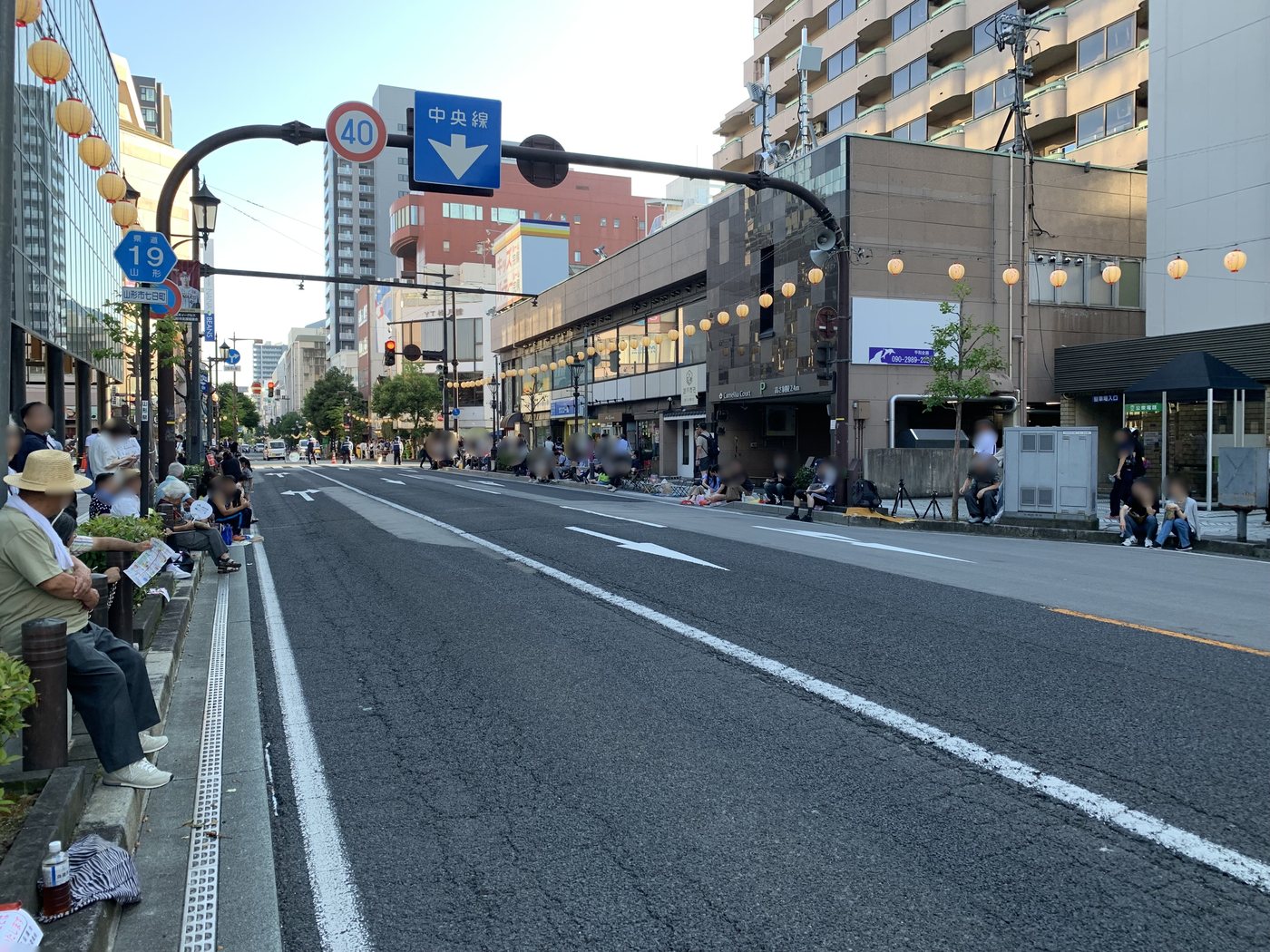 昼間の沿道。歩道に座って場所取りをしている人がまばらにいる
