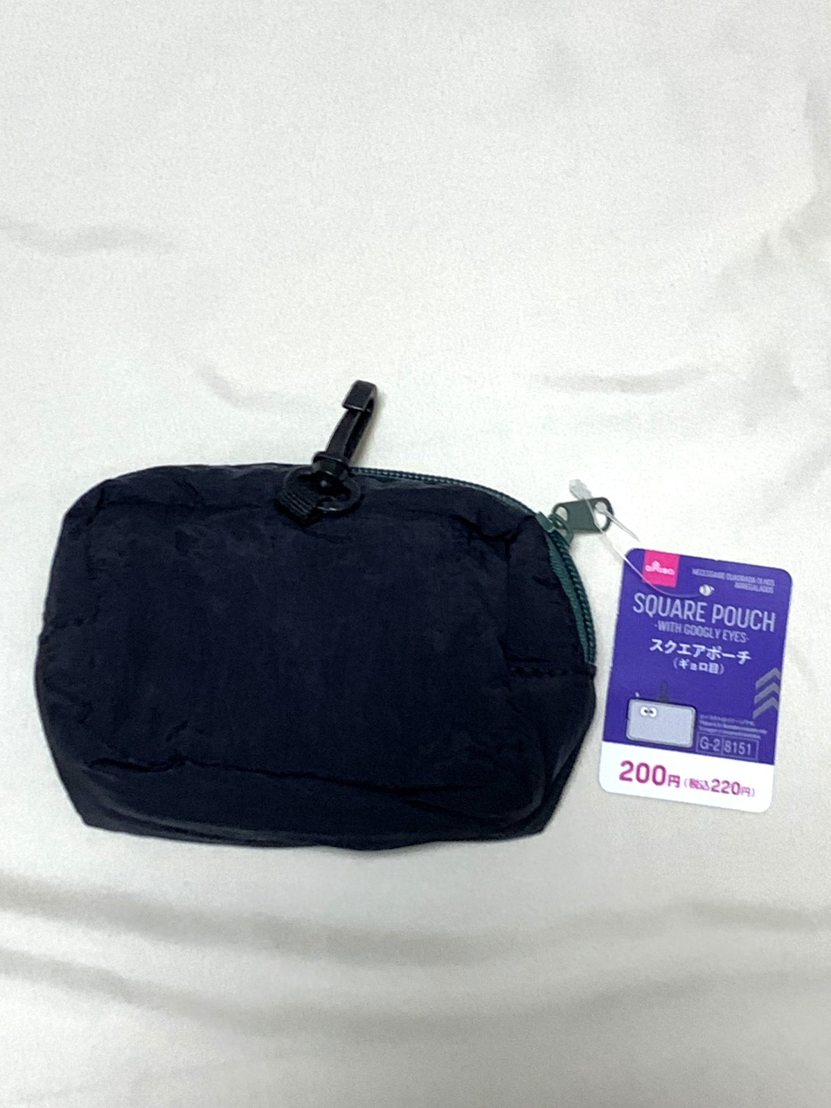 スクエアポーチの裏面と値札。値札にはSQUARE POUCH WITH GOOGLY EYES スクエアポーチ ギョロ目 200円税込220円と書かれている
